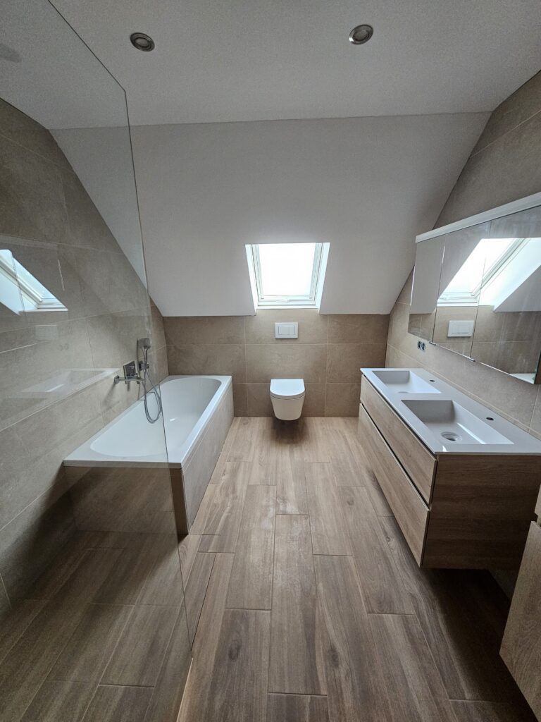 Modern saniertes Badezimmer mit Doppelwaschbecken, Badewanne und Toilette unter dem Fenster.